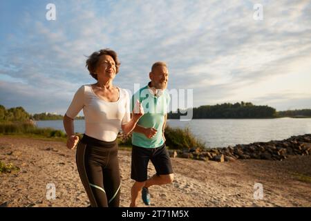 Happy elderly couple running on beach enjoying jogging workout in morning Stock Photo