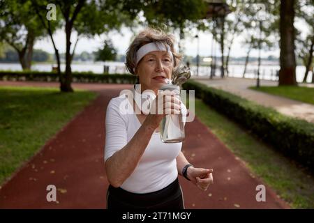 Elderly woman drinking water taking short break during running exercise Stock Photo