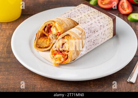 Chicken wrap with vegetables on a white porcelain plate on wooden table Stock Photo