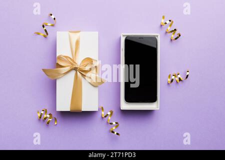 Opened gift box with gold ribbon and smartphone on color background, top view. Blank open box packaging mockup , Template for your design - branding m Stock Photo