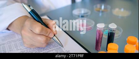 Banner of unrecognizable female scientist hand filling investigation form about dangers of small plastic particles on glitter. Close up of woman chemi Stock Photo