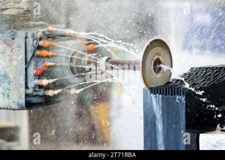 Working on a design of a large block of Black Italian Carrara marble in a workshop using a water cooled orbital saw in a close up on the blade and spr Stock Photo