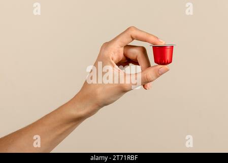 From above of anonymous young female holding coffee capsule in manicured slender index and thumb fingers and demonstrating against beige background Stock Photo