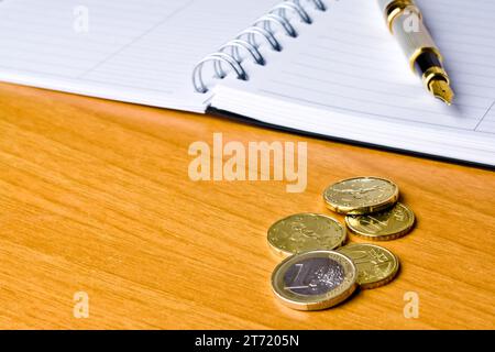 detail of coin and ink pen on notebook on wood table Stock Photo