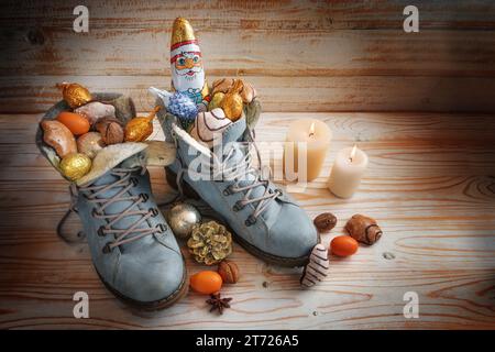 Boots filled with sweets, chocolate Santa and Christmas decoration on a wooden background with candles, tradition on German Nikolaus Tag meaning Nicho Stock Photo