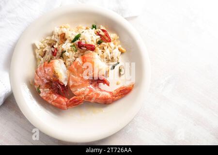 Large prawns or shrimps with spicy rice, garlic, red chili pepper and herbs on a white plate and a light background, homemade seafood meal, top view f Stock Photo