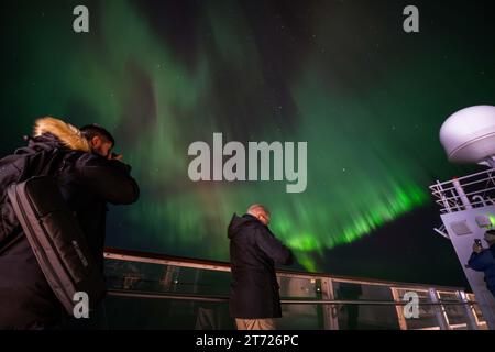 Several people are seen taking pictures during an aurora borellae apparition in the skies near Bøøyna, Norway. Northern lights are natural phenomena that illuminate the night sky in the polar regions. Produced by the interaction of charged solar particles with the Earth's atmosphere, they create colorful, dancing flashes of light in shades of green, pink and purple. This celestial spectacle is the result of the excitation of atoms and molecules in the upper atmosphere, generating a visually stunning effect. Credit: SOPA Images Limited/Alamy Live News Stock Photo