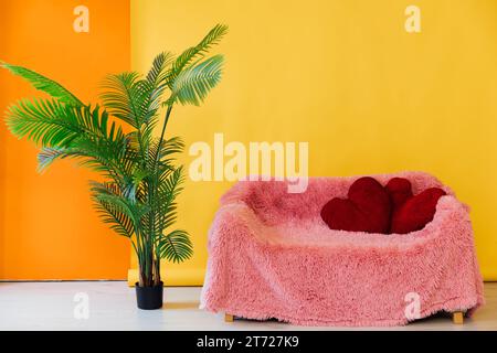 pink sofa with red pillows and decorative flower on a yellow background Stock Photo