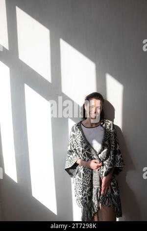 a woman stands on a white background in the shade from the window Stock Photo