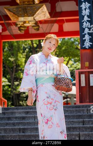 Portrait of a young woman wearing Japanese yukata summer kimono standing in front of the shrine gate. Kyoto, Japan. Stock Photo