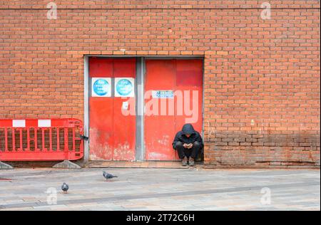 London, UK. Man sitting in a doorway in Chinatown, looking at his phone Stock Photo