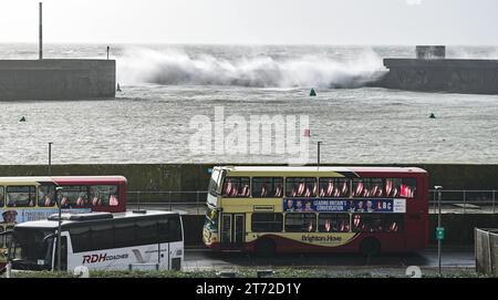 Brighton UK 13th November 2023 - A bus passes by as waves crash over Brighton Marina wall as Storm Debi approaches Britain with weather warnings being issued for parts of the country : Credit Simon Dack / Alamy Live News Stock Photo