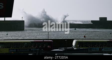 Brighton UK 13th November 2023 - A bus passes by as waves crash over Brighton Marina wall as Storm Debi approaches Britain with weather warnings being issued for parts of the country : Credit Simon Dack / Alamy Live News Stock Photo