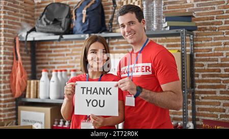 Man and woman volunteers standing together holding paper with thank you message at charity center Stock Photo