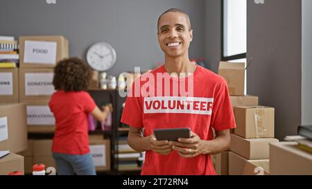 Smiling man and woman volunteers using touchpad together at charity center, strengthening community through altruism and digital activism Stock Photo