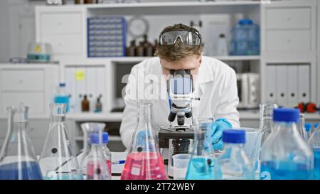 Handsome young caucasian man, a dedicated scientist, deeply engrossed in analyzing samples under the microscope at a professional medical lab. Stock Photo