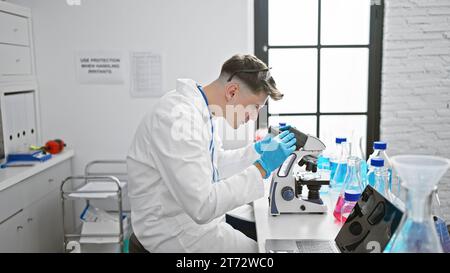 Handsome young caucasian man, a dedicated scientist, deeply engrossed in analyzing samples under the microscope at a professional medical lab. Stock Photo
