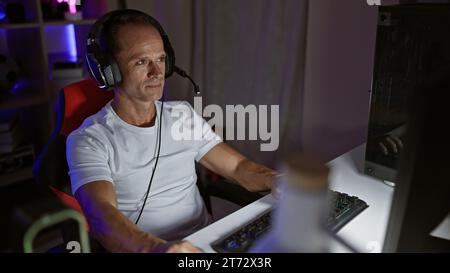 Handsome middle age man streaming video game at night, sitting seriously concentrated at his cyber gaming room, fully equipped with futuristic technol Stock Photo