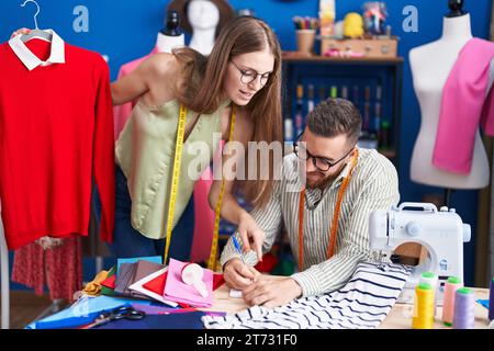Man and woman tailors holding t shirt writing on notebook at clothing factory Stock Photo