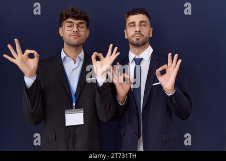 Two hispanic business men wearing business clothes relax and smiling with eyes closed doing meditation gesture with fingers. yoga concept. Stock Photo