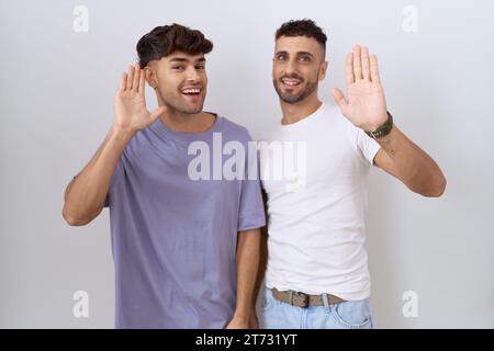 Homosexual gay couple standing over white background waiving saying hello happy and smiling, friendly welcome gesture Stock Photo