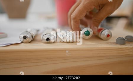 Attractive young hispanic man, a grey-haired artist, is holding a tube of color in art studio, exploring his creativity and painting lessons Stock Photo