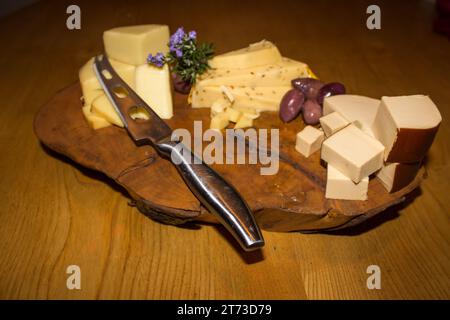 A wooden cheese plate with three different types of cheeses and olives, Stock Photo