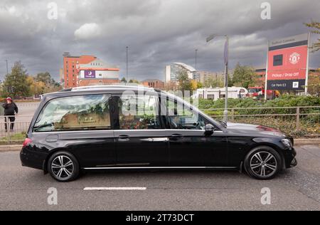 Manchester, UK. 13 November, 2023. Sir Bobby Charlton's hearse passes Old Trafford Football ground where flowers and messages had been left at the memorial to the 1958 Munich disaster. The Hearse left passed the Trinity Statue and left via Sir Matt Busby way to make its way to the funeral held in Manchester city centre. Picture: garyroberts/worldwidefeatures.com Credit: GaryRobertsphotography/Alamy Live News Stock Photo