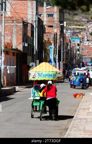 A woman and her daughter push a tricycle cart selling ceviche (raw, marinated fish, a famous typical Peruvian dish) along a street in Puno, Peru Stock Photo