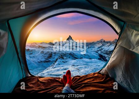 Woman cross leg on blanket in camping tent with sleeping bags on mountain hill. view from inside with Matterhorn mountains. Stock Photo
