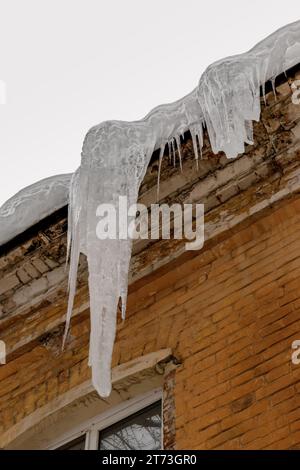 A huge icicle (block of ice) hanging from the roof of a brick building. Stock Photo