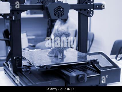 Model of toy lion printed on 3D printer from melted plastic blue color on desktop of 3D printer. Concept 3D printer, 3D printing, modeling prototyping three dimensional object. Innovative production Stock Photo