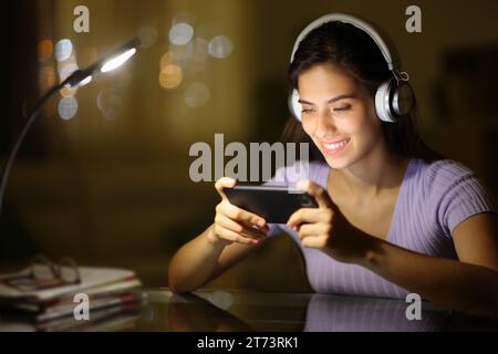 Happy woman wearing headphone in the night watching videos on phone at home Stock Photo