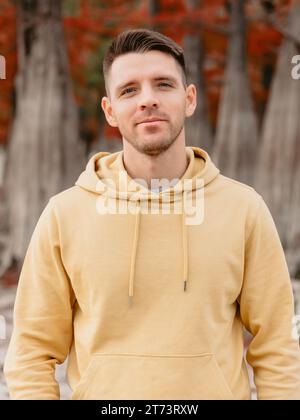 Handsome man looking at camera in autumnal forest. Caucasian young man in yellow hoodies Stock Photo