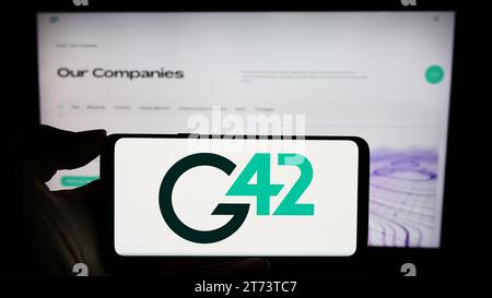 Person holding mobile phone with logo of Emirati technology company Group 42 Holding Ltd. (G42) in front of web page. Focus on phone display. Stock Photo