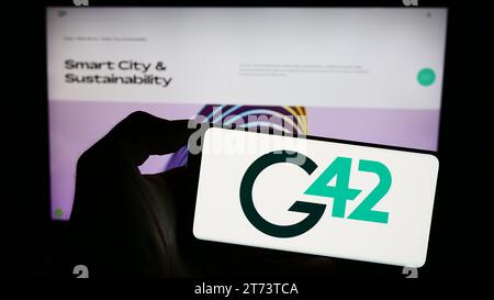 Person holding cellphone with logo of Emirati technology company Group 42 Holding Ltd. (G42) in front of webpage. Focus on phone display. Stock Photo
