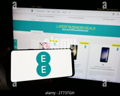 Person holding mobile phone with logo of British telecommunications company EE Limited in front of business web page. Focus on phone display. Stock Photo