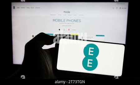 Person holding cellphone with logo of British telecommunications company EE Limited in front of business webpage. Focus on phone display. Stock Photo