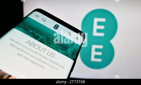 Mobile phone with website of British telecommunications company EE Limited in front of business logo. Focus on top-left of phone display. Stock Photo