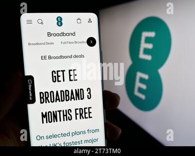 Person holding cellphone with web page of British telecommunications company EE Limited in front of logo. Focus on center of phone display. Stock Photo