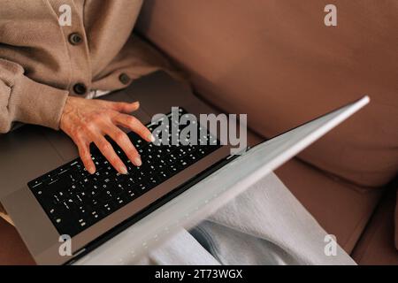 Closeup high-angle view of unrecognizable middle-aged woman using laptop, typing on keyboard, writing email or message in social network Stock Photo