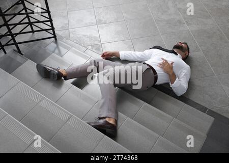 Unconscious man lying on floor after falling down stairs indoors Stock Photo