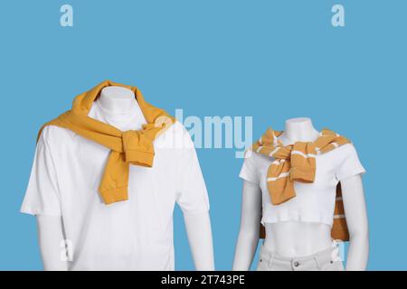 Female and male mannequins dressed in white t-shirts and orange sweaters on light blue background Stock Photo