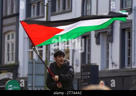 Young muslim man tood up high waving his flag at the Pro Palestine March in Cardiff City Centre, Saturday 11th November 2023 Stock Photo