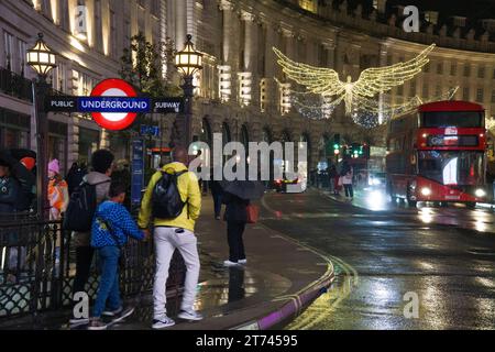 UK weather, London, 12 November 2023: Christmas lights on Regent Street are reflected from wet roads on a rainy night, with one of the entrances to Piccadilly underground station on the left. Anna Watson/Alamy Live News Stock Photo