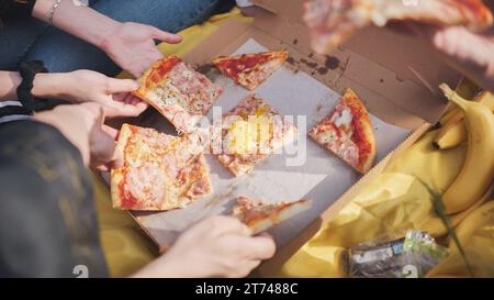 Young students' hands reach for the pizza. Stock Photo