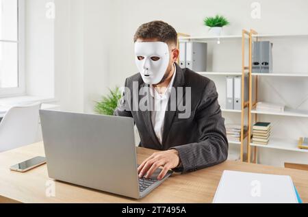 Anonymous man in face mask uses laptop computer for online business or internet scam Stock Photo