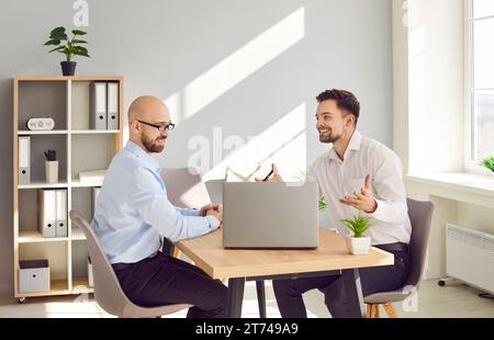Two smiling businessmen chatting while sitting at laptop in office Stock Photo