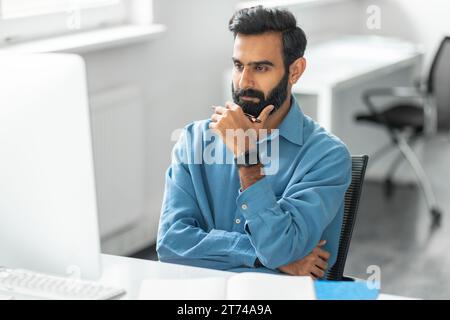 Thoughtful indian man with beard looking at computer Stock Photo