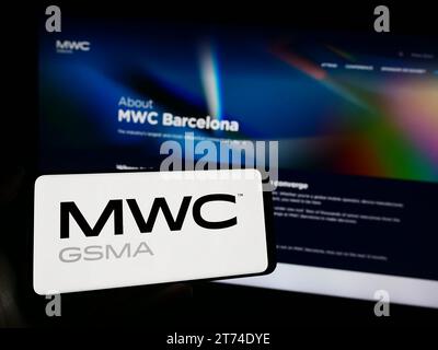 Person holding smartphone with logo of annual mobile communications trade show MWC Barcelona in front of website. Focus on phone display. Stock Photo